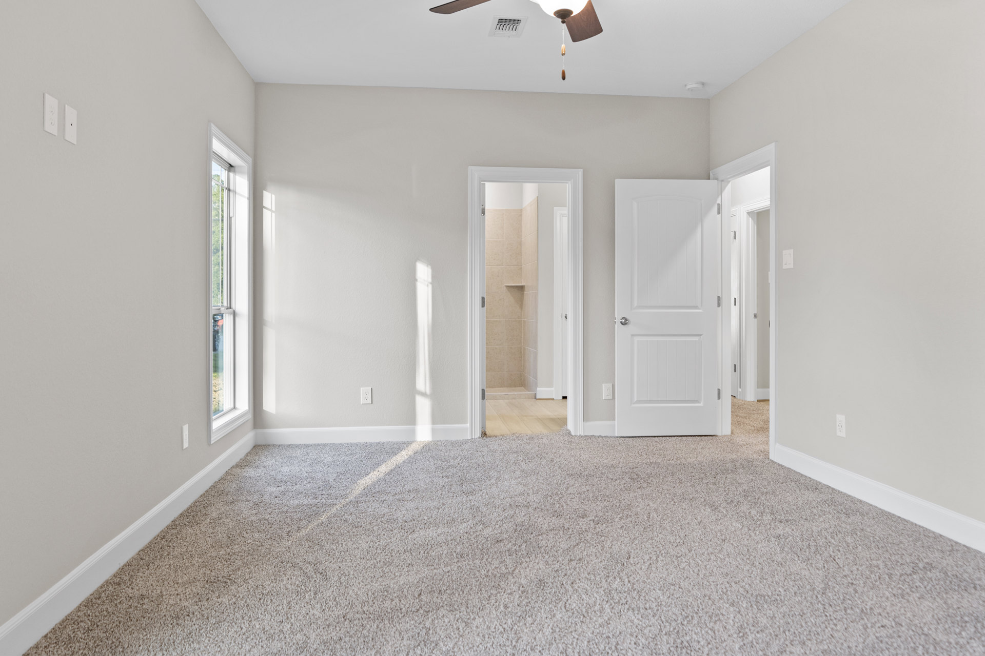 Carpeted room with white walls, ceiling fan, open white door with silver knob, ceiling vent, and window partially visible
