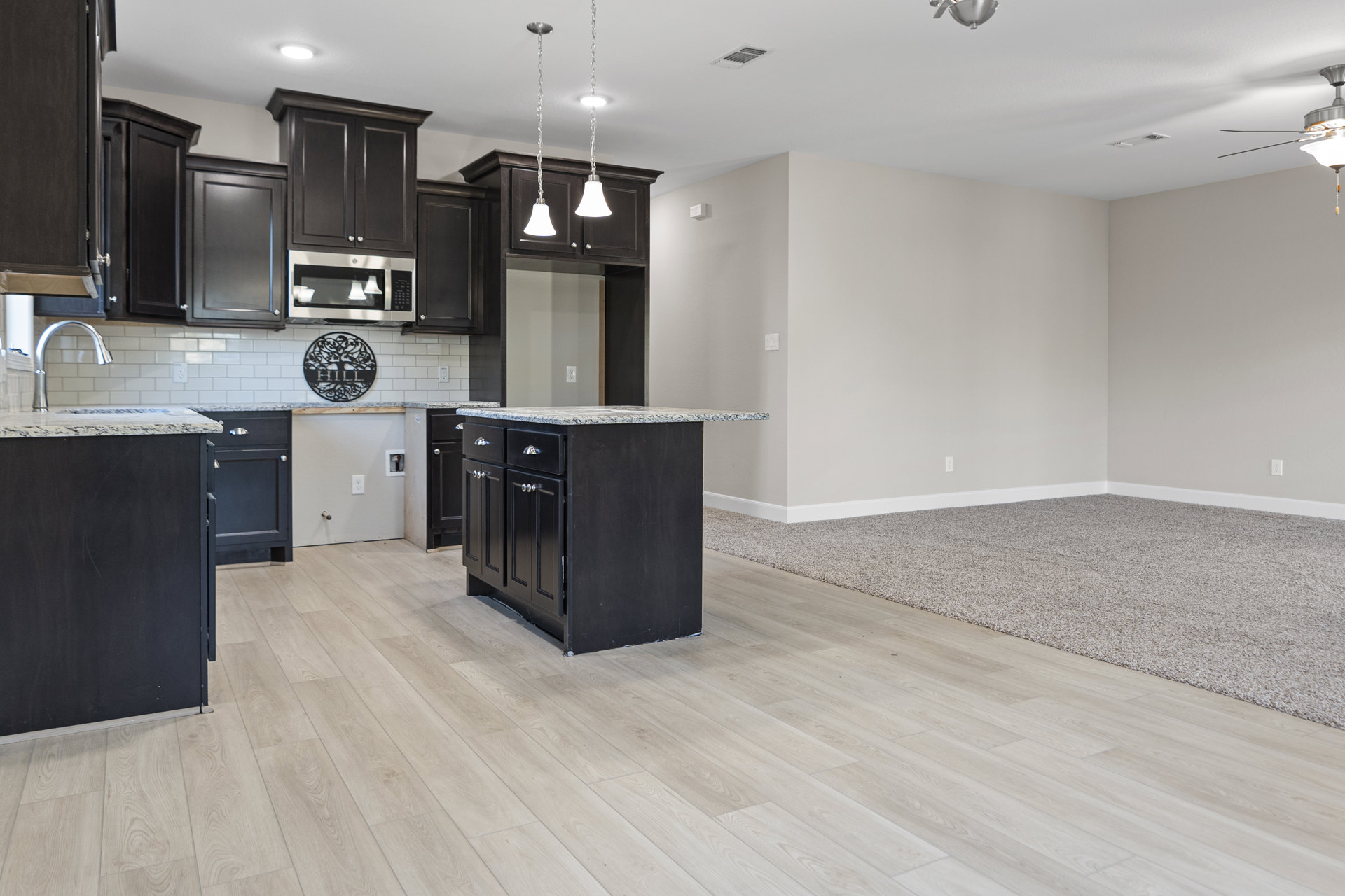 Open kitchen and living room with hardwood floors, white tile backsplash, black kitchen island topped with marble, built-in microwave, modern cabinetry, and recessed lighting