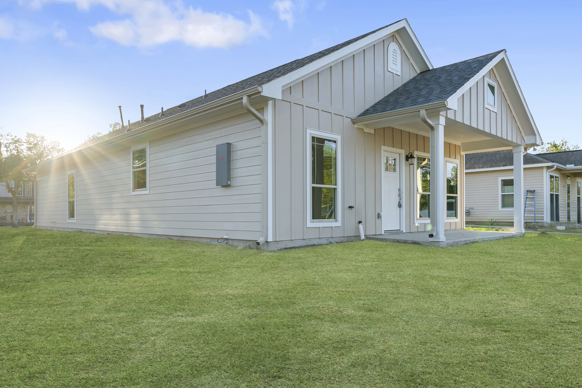 Two-story house with white framed windows, white front door, manicured green lawn, porch, and blue sky with scattered clouds