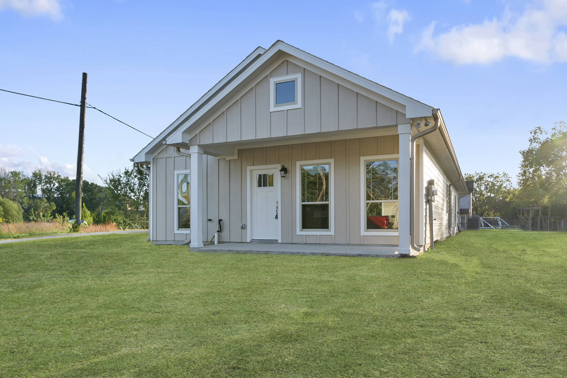 Modern two-story home with white door and large windows, surrounded by green lawn and mature trees, under partly cloudy sky