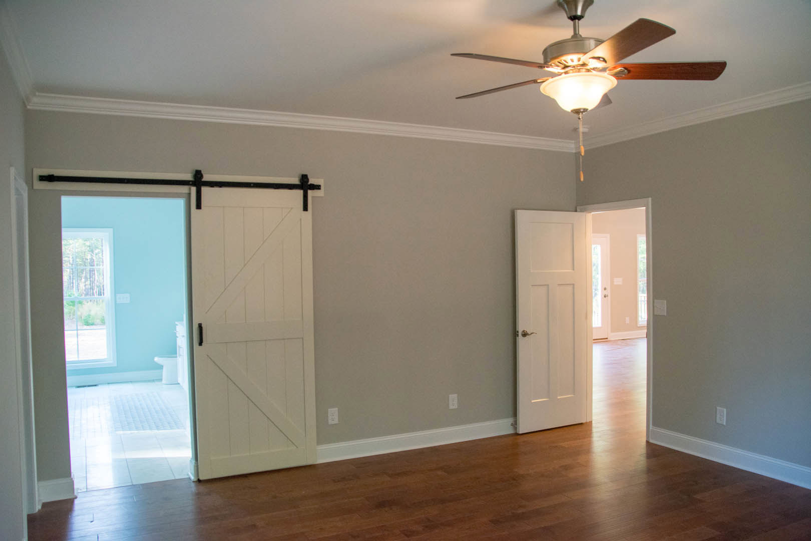 Ceiling fan with light fixture in a room featuring two white doors, one with a black handle, sliding door detail, neutral walls, and window.