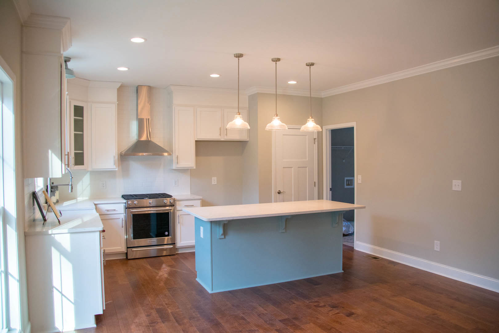 Modern kitchen featuring a central island with white countertop, stainless steel stove with black oven window, white cabinetry, metal backsplash, overhead light fixture, and large