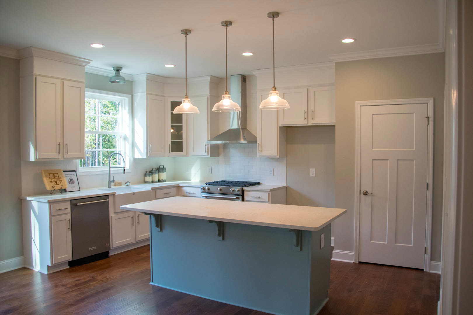Modern kitchen featuring a central island with stone countertop, stainless steel stove, white cabinetry, tile backsplash, and silver hardware.