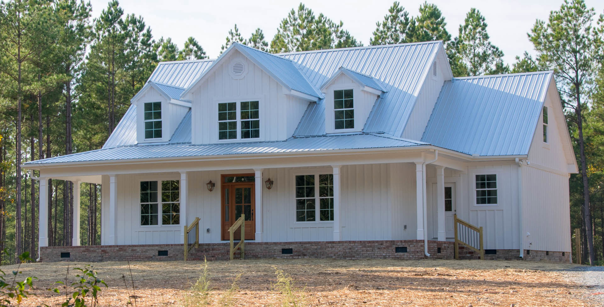 White siding house with blue metal roof, wooden porch railing with black metal bars, white-framed windows, and white vent on exterior wall