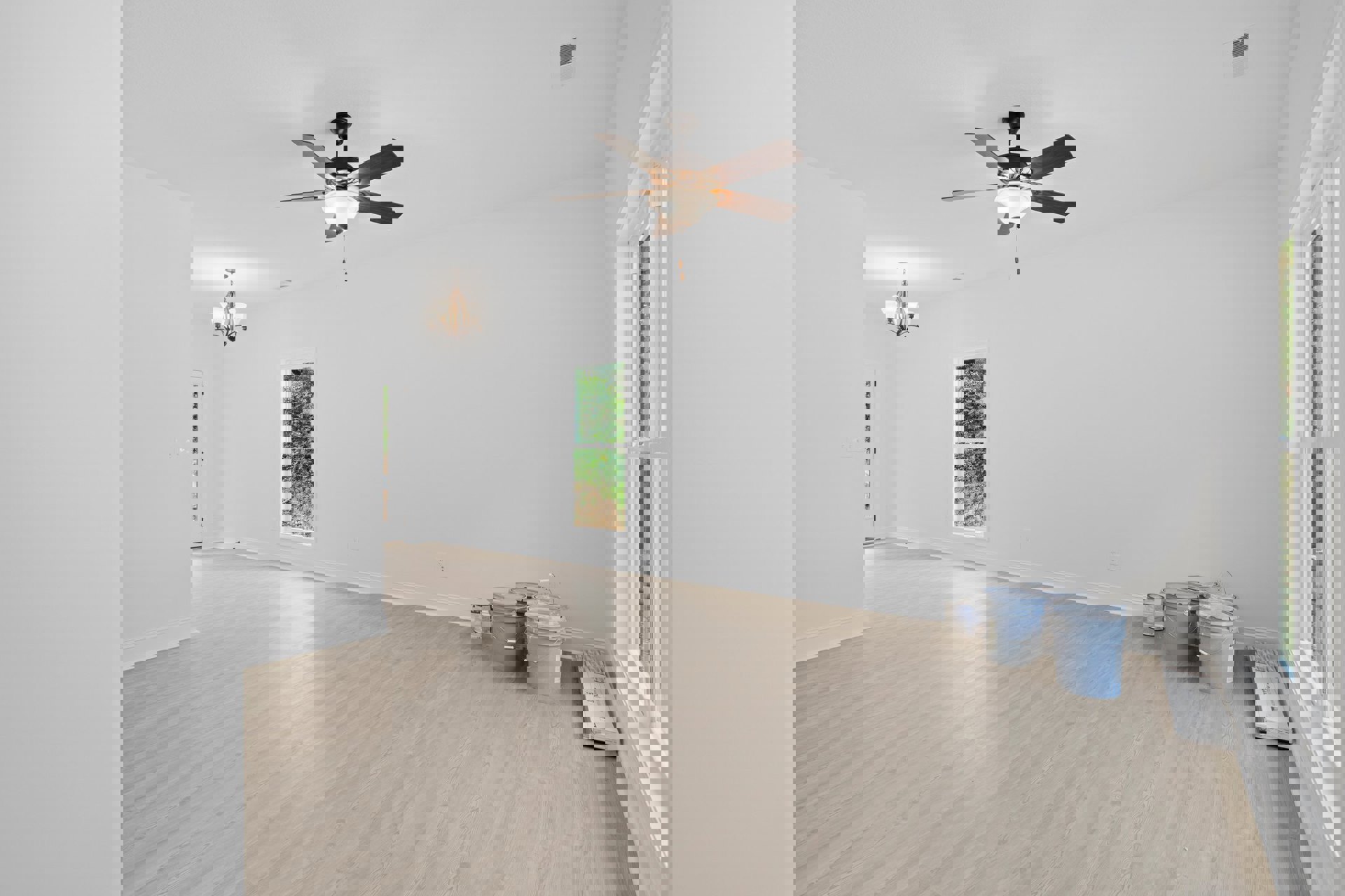 Ceiling fan with light fixture above laminate wood flooring, white framed window, several plastic buckets, and a white box with keyboard in a plaster-walled room