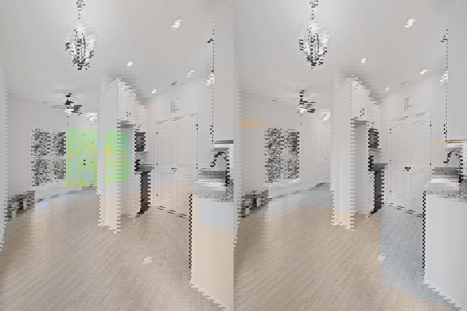 White kitchen with wood flooring, ceiling fan, black microwave built into white cabinetry, window overlooking trees, white light fixture, and chandelier with white glass shades.