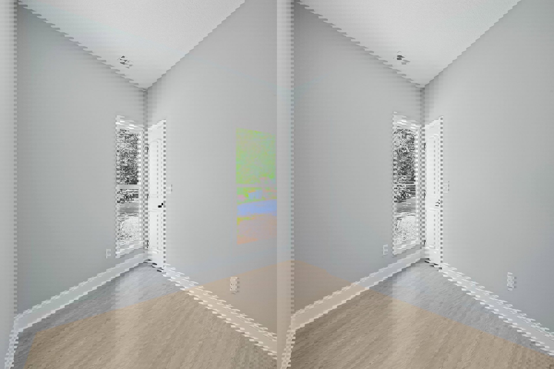 Wood floor room with white door featuring black knob, large window with white frame, view of tree-lined path and street outside