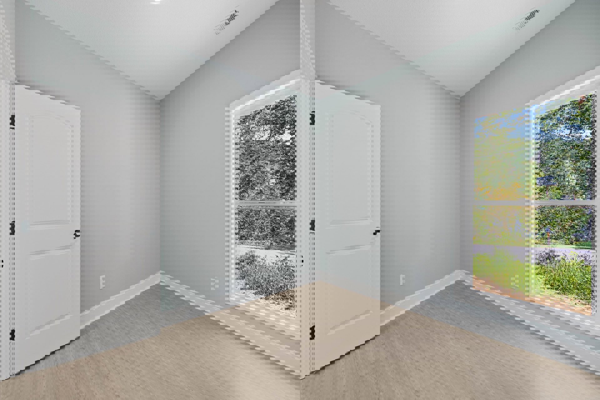 Wood floor with white baseboards, white door with black knobs, window showing trees and power lines, white walls and ceiling