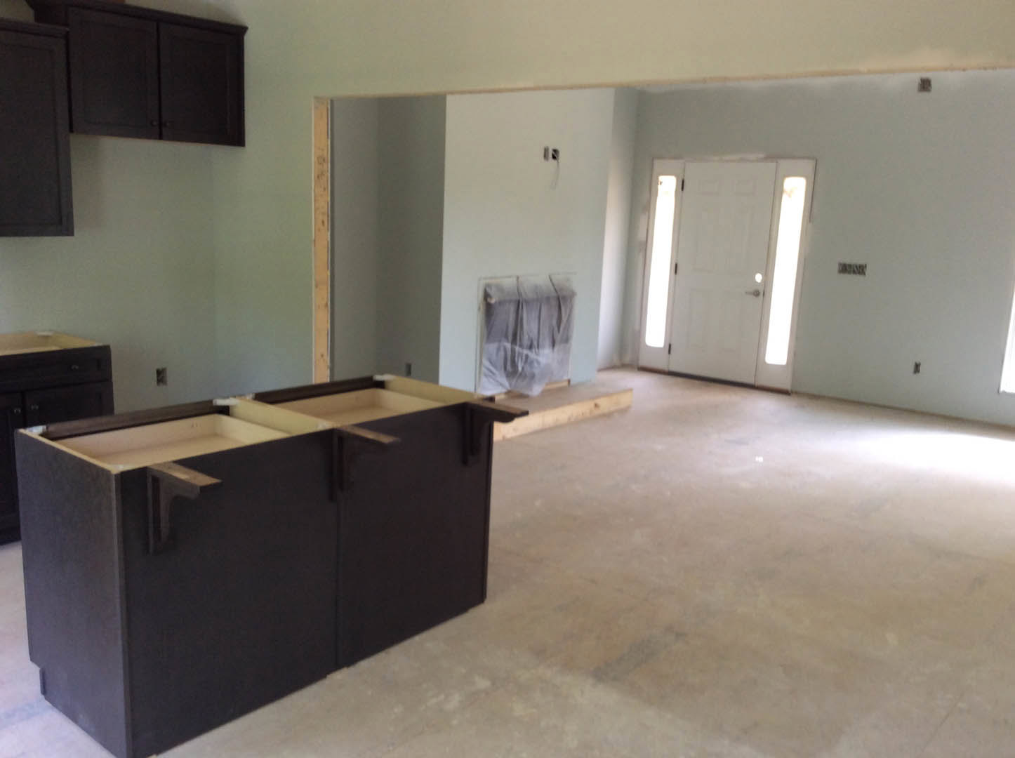 Modern kitchen featuring black countertop, black cabinetry with two drawers, white door with glass panels, light flooring, and stainless steel appliances.