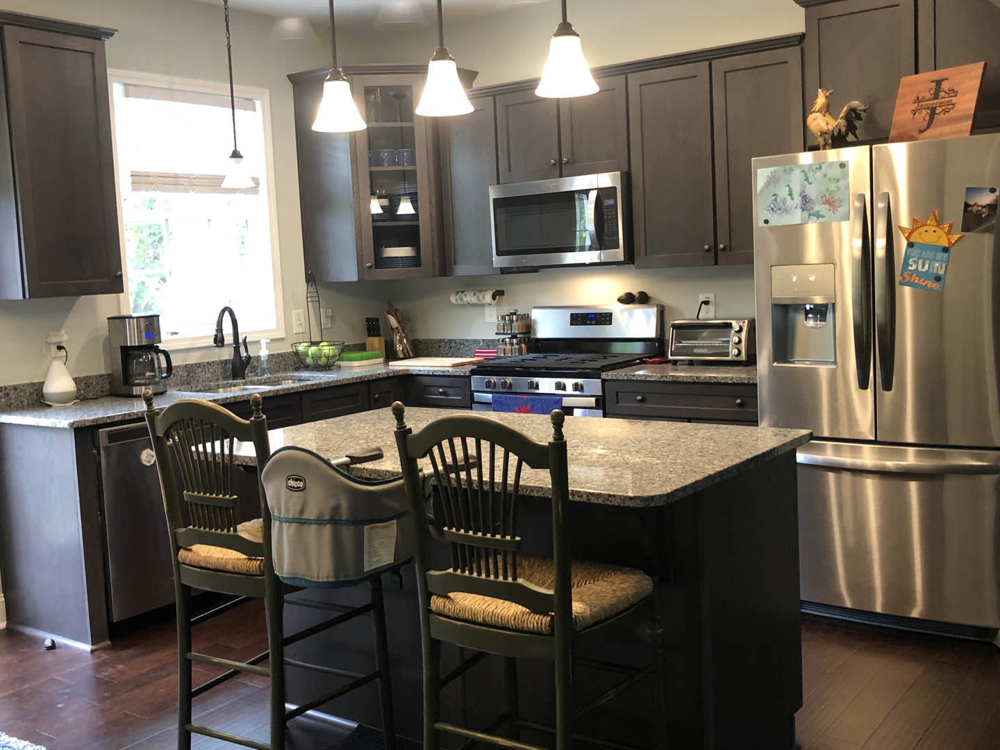 Modern kitchen featuring a bar-height counter with two chairs, stainless steel refrigerator with water dispenser, built-in microwave above stove, white cabinetry, stone