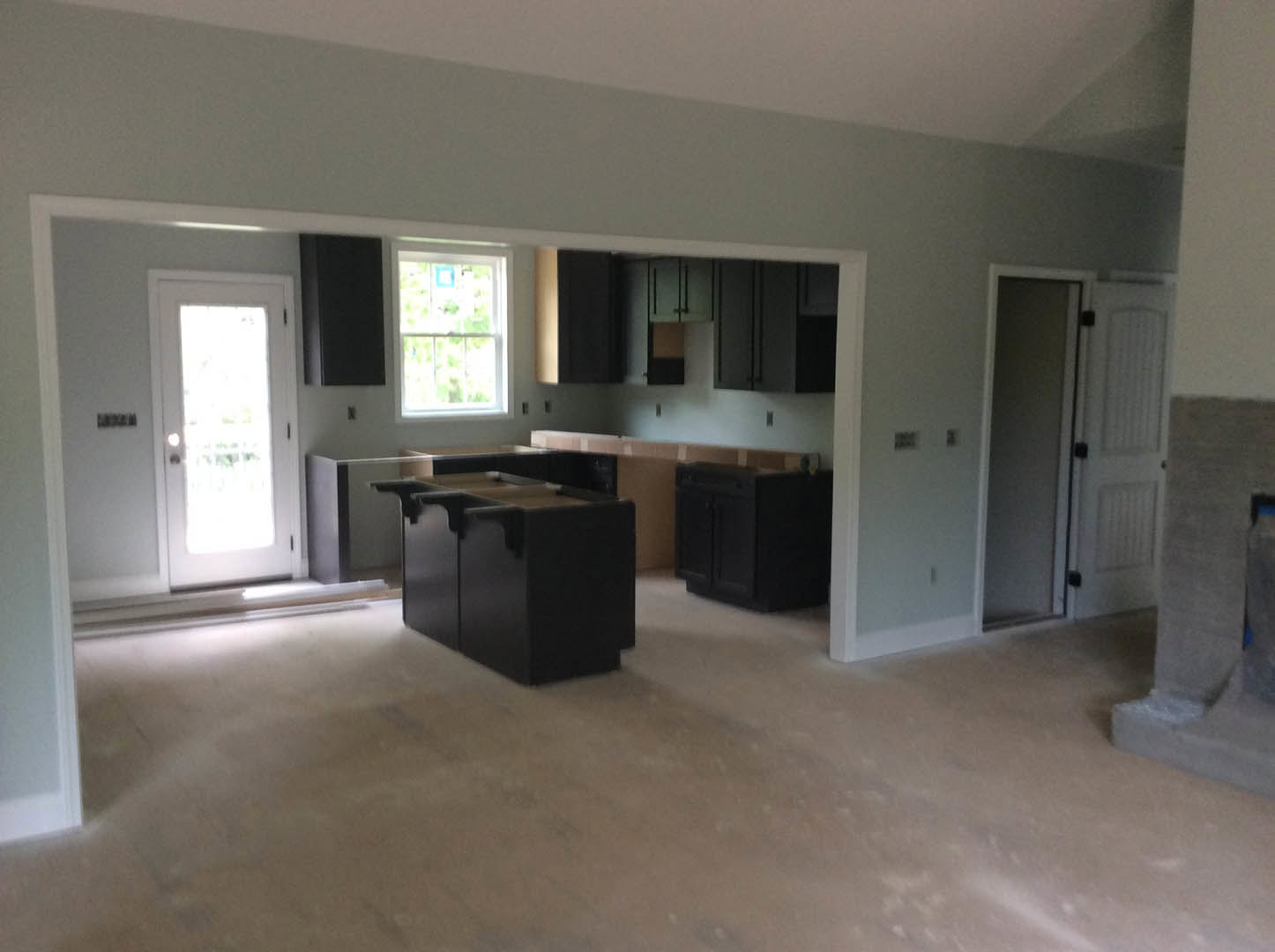 Modern kitchen with white cabinetry, black hardware, large window with white frame, glass-paneled door, light wood flooring, and sleek black storage box on countertop