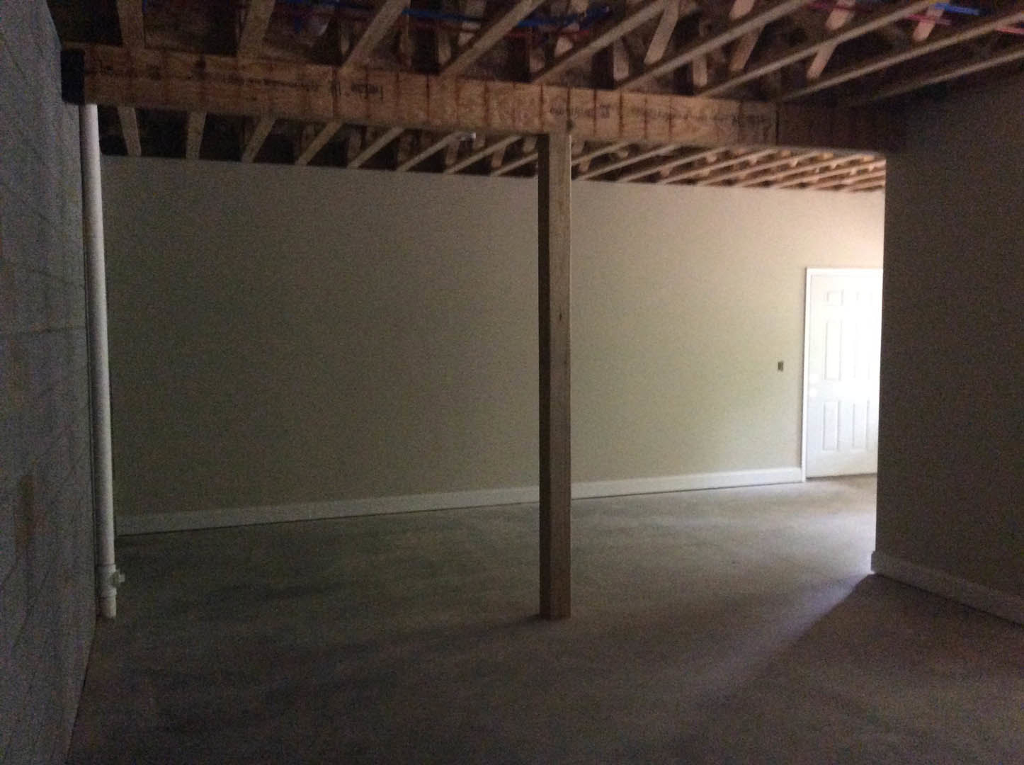 Open room with exposed wooden ceiling beam, white plaster walls, white door, partial brick accent, black wall with white trim, and table leg visible on hardwood floor