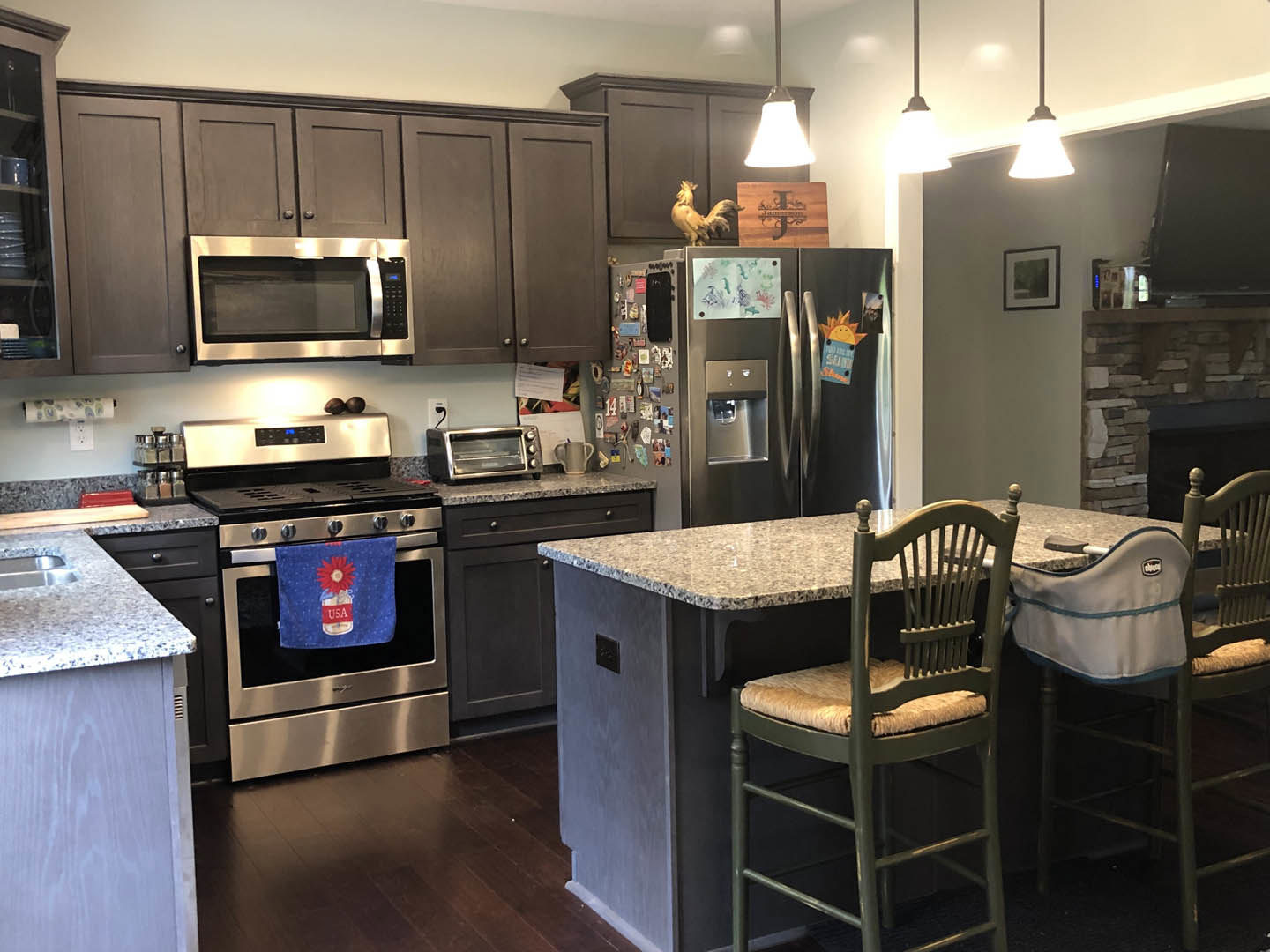 Modern kitchen featuring a bar with seating, stainless steel refrigerator, white cabinetry, built-in microwave, towel draped over stove, blue floral towel, and toaster oven on
