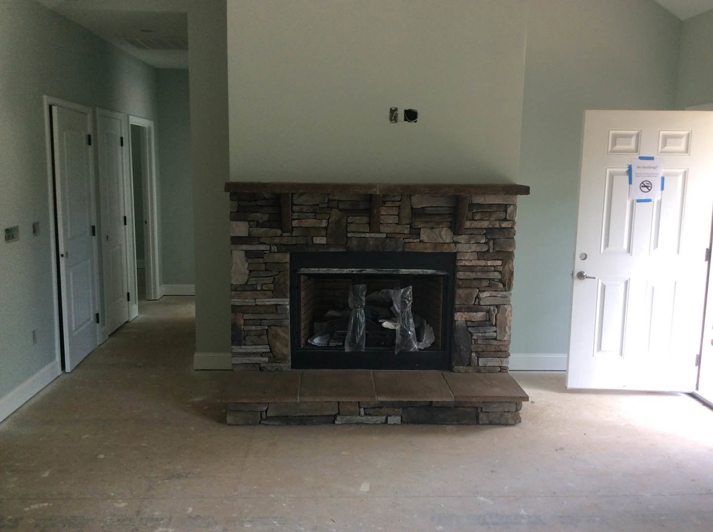 Stone fireplace with plastic bags inside, white door with black hinges and no smoking sign, light-colored walls and ceiling, hardwood floor