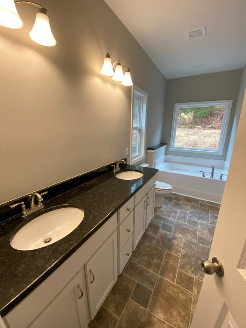 White freestanding bathtub beside a large window overlooking a grassy field, modern vanity with vessel sink and chrome faucet, marble tile flooring, three-bulb light fixture above