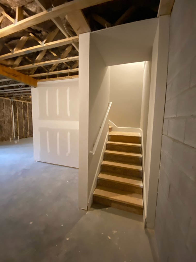 Wood staircase with unfinished plaster walls, exposed beams, and construction materials scattered on the floor in a partially built interior.