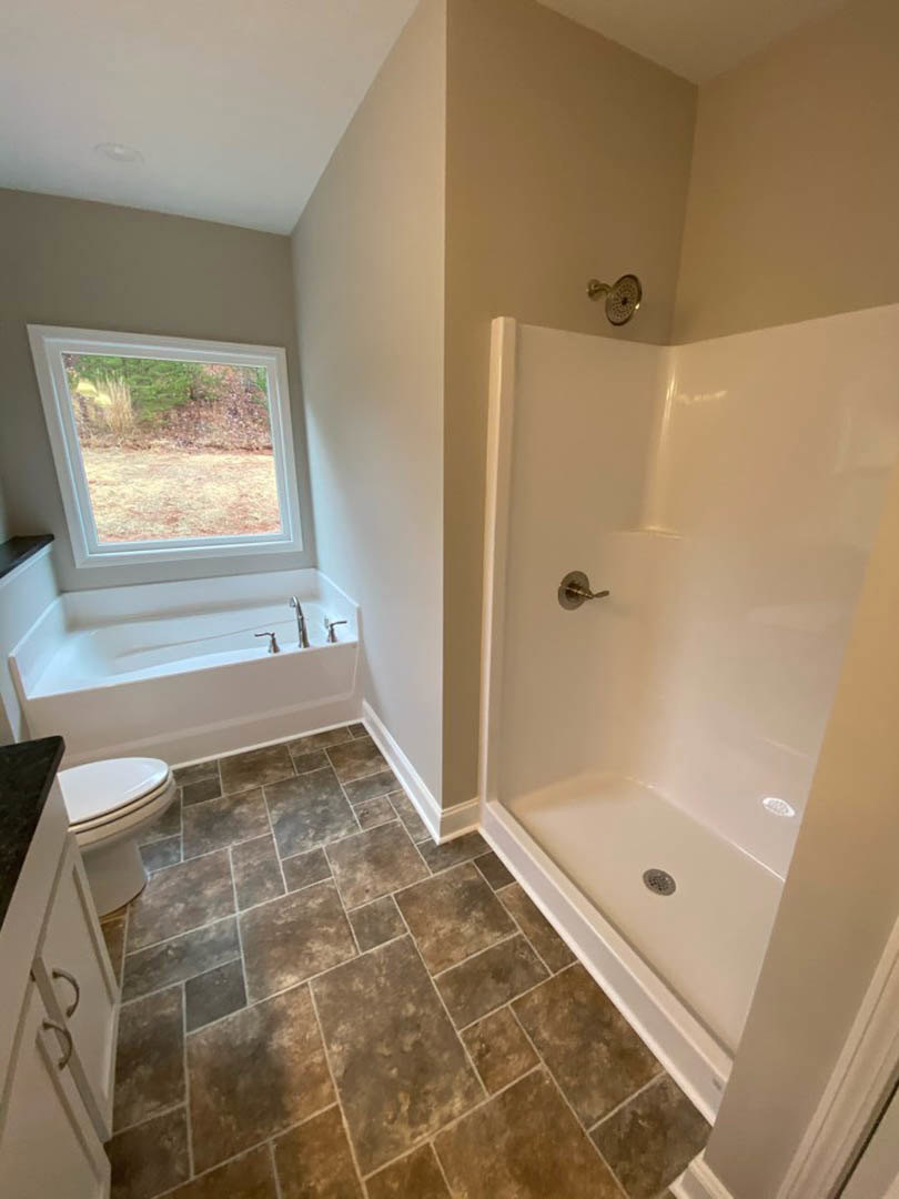 Bathroom with large tile floor, glass-enclosed shower, white toilet, and window overlooking grassy field