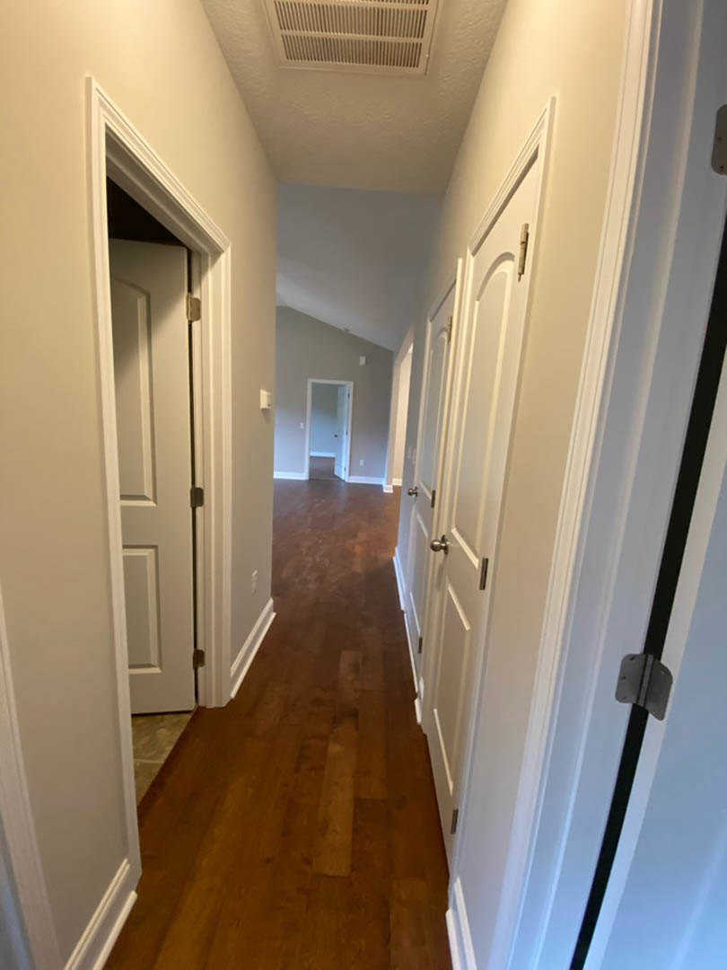 Hallway with white paneled doors, light hardwood flooring, white baseboards, and a metal door hinge visible on a close door