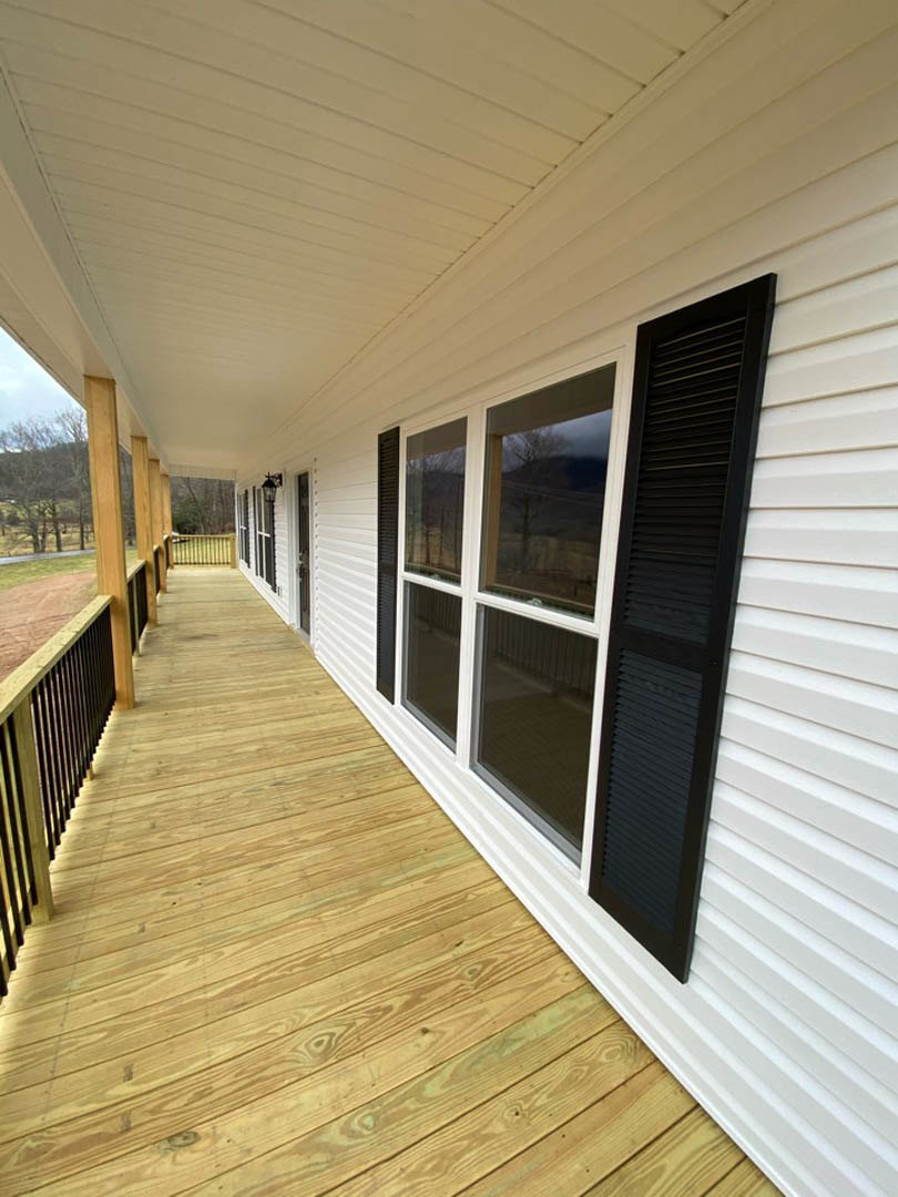 White siding exterior with black shutters, black metal porch railing, wood plank deck, and multiple windows