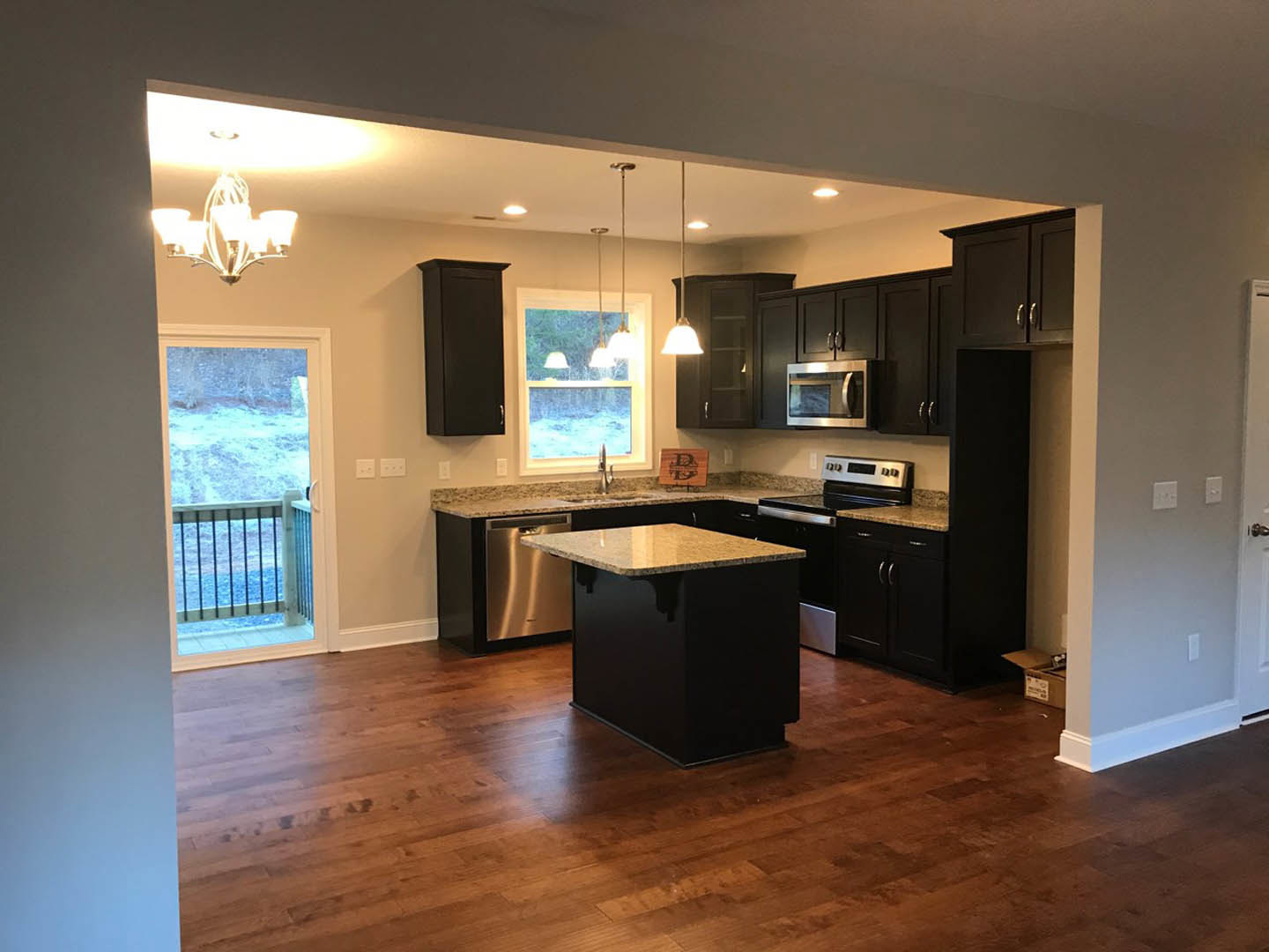 Kitchen with light wood flooring, marble-topped island, white cabinetry, stainless steel microwave, open door revealing snowy outdoors, decorative wooden sign on wall