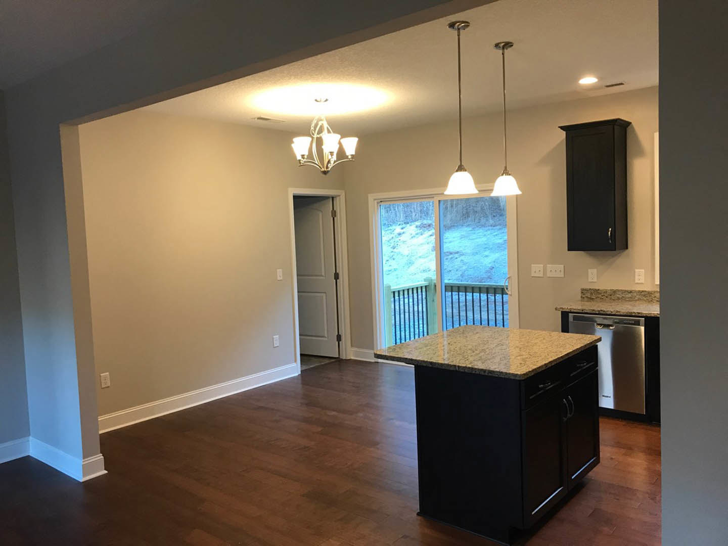 Kitchen with wood flooring, central island featuring marble countertop, white cabinetry, stainless steel dishwasher, white door with black handle, sliding glass door overlooking