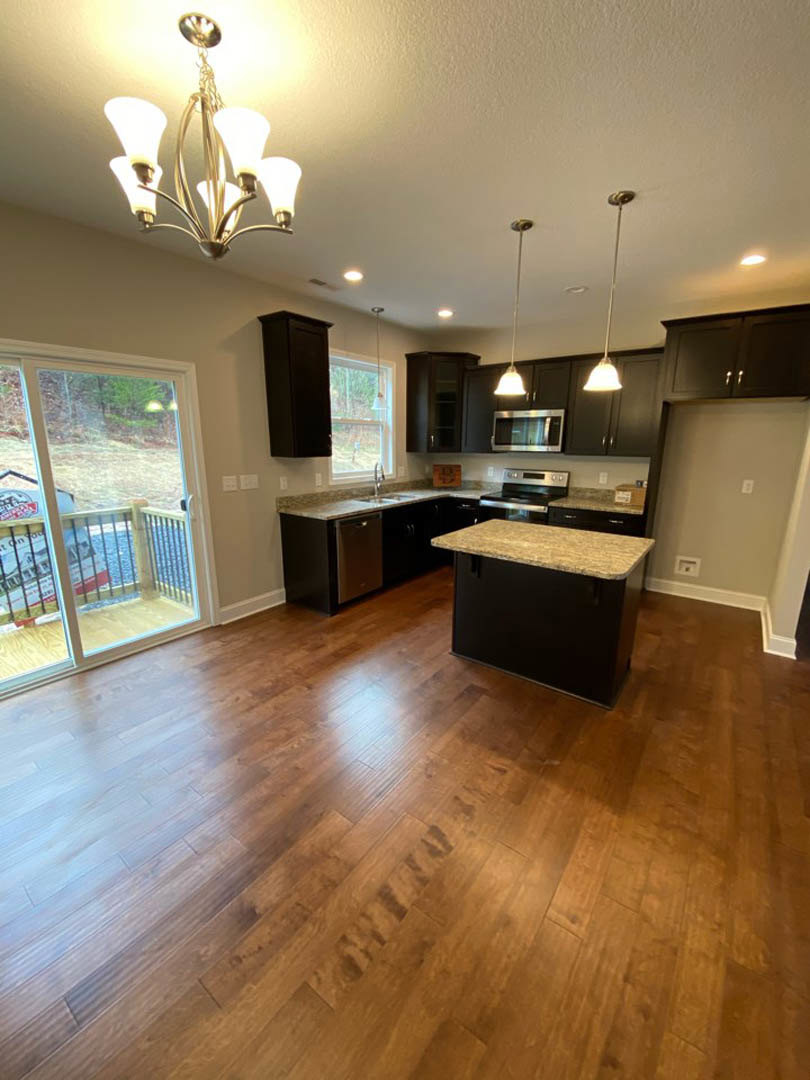 Hardwood kitchen floor with dark island, cabinetry, chandelier, glass door with railing, and countertop; stove visible in background