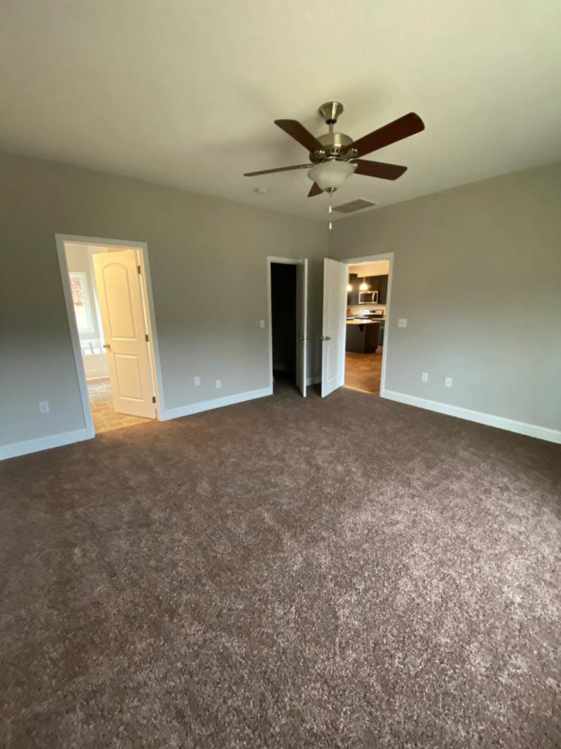 Carpeted room with white walls, ceiling fan with light, open white door letting in sunlight, black door with white frame, doorway leading to kitchen