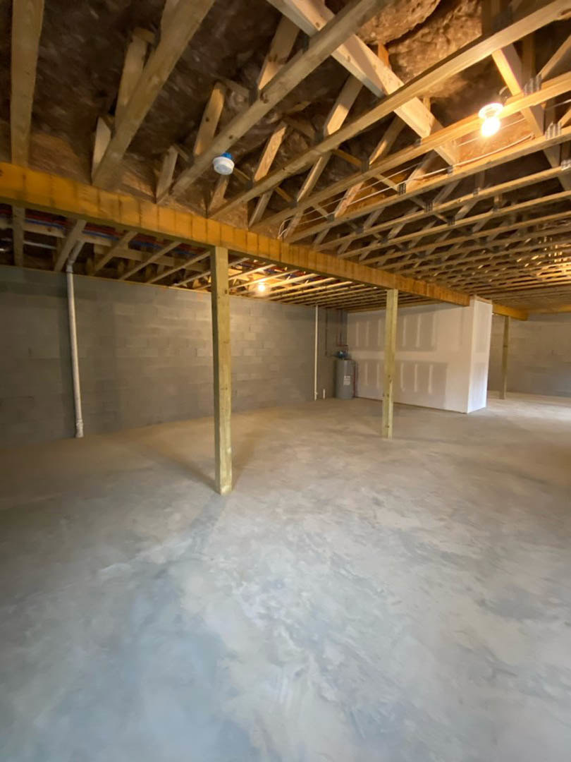 Open room with exposed wooden ceiling beams, concrete floor, white walls, and a wooden post featuring a yellow stripe