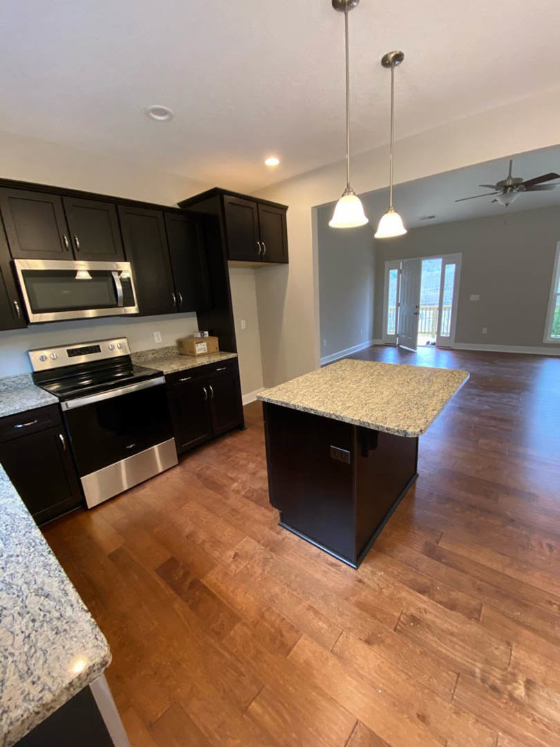 Marble kitchen island with waterfall edge, wood plank flooring, black and silver stove, white cabinetry, modern pendant lighting, and stainless steel appliances