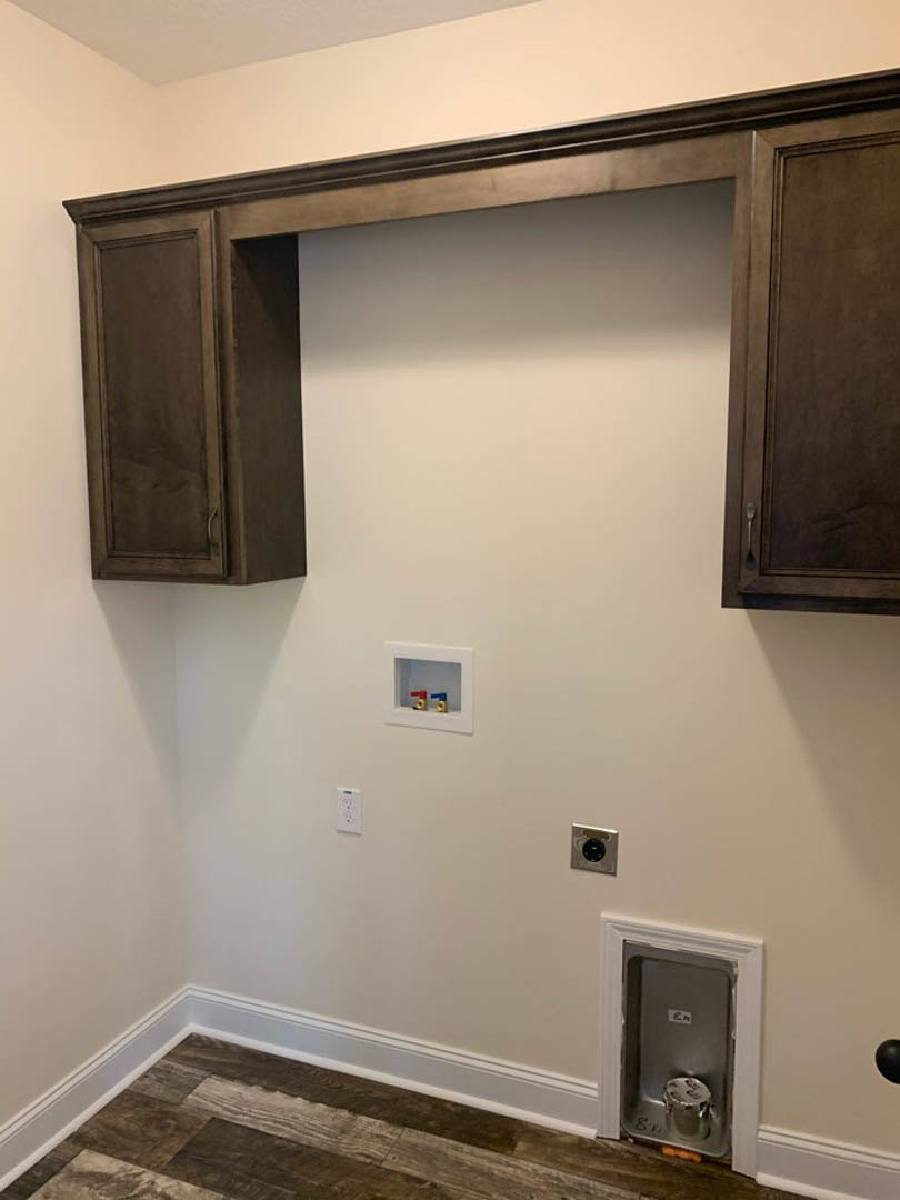 Modern kitchen featuring wood flooring with white baseboards, white cabinetry, built-in dryer vent with black circular cover on a silver square, and small plastic toy pipes