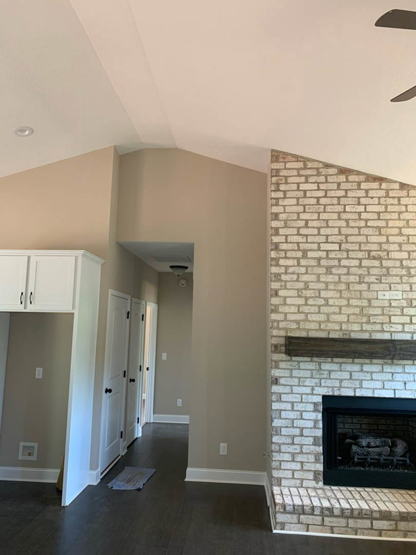 Stone tile fireplace with stacked logs, wooden mantel shelf, white door with black hardware, light wood flooring, and white towel folded on nearby table
