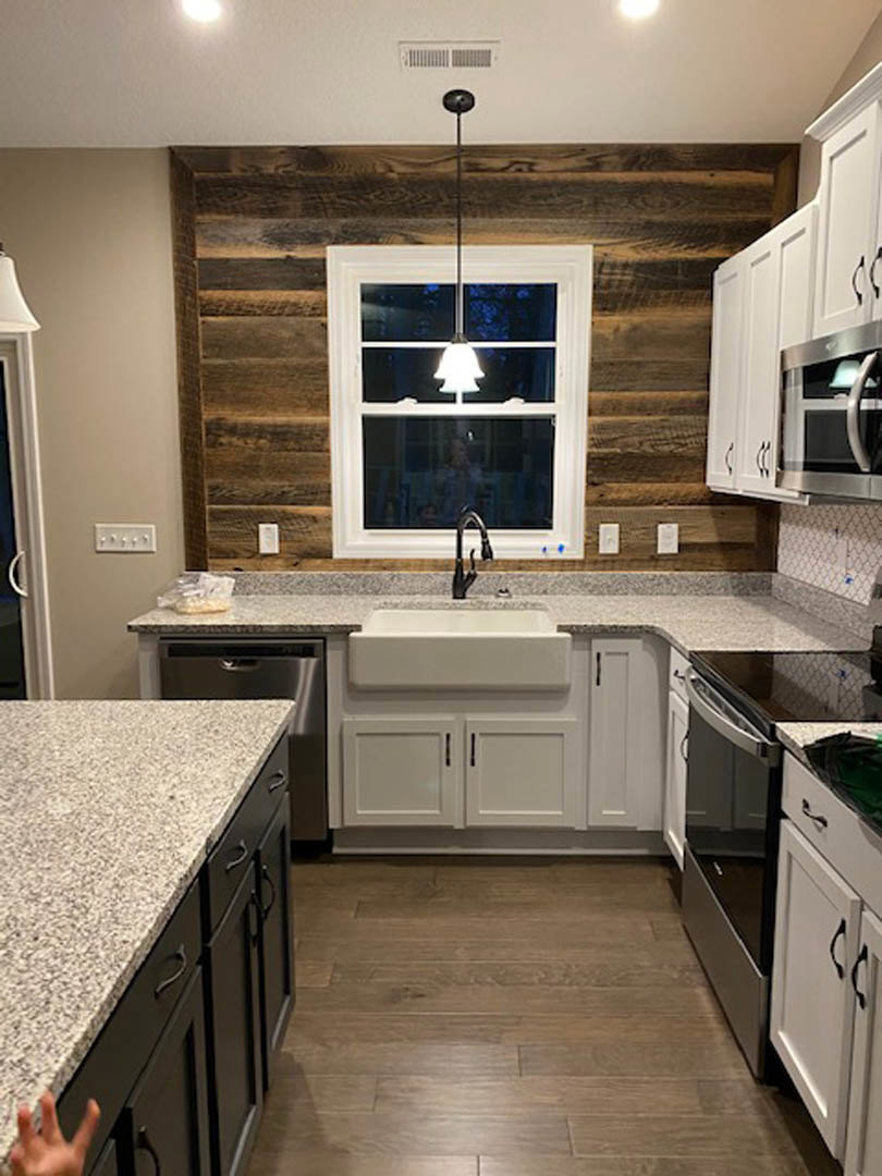 Kitchen featuring wood paneled accent wall, window above sink, white cabinets with black handles, and light-colored countertop