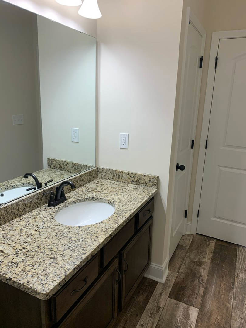 Marble countertop with undermount sink, chrome faucet, large framed mirror, wood flooring, white door with black handle, tile backsplash