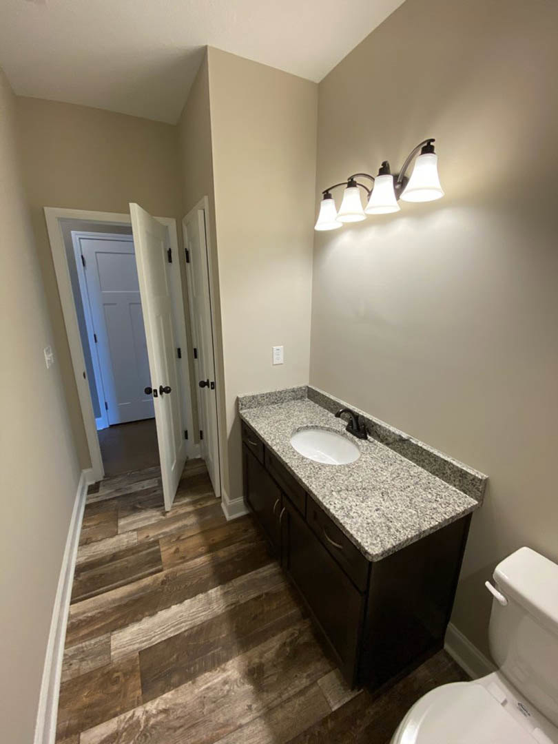 Bathroom with marble countertop, white sink, wood flooring, wall-mounted mirror, and chrome faucet
