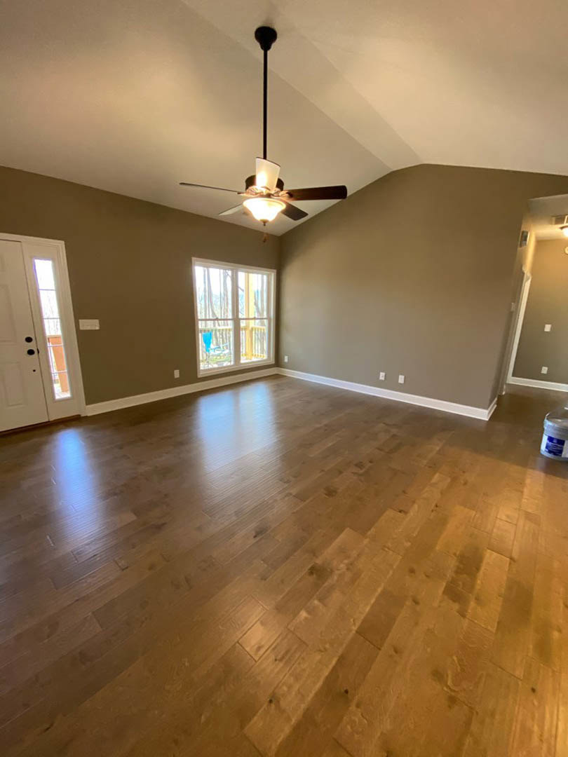 Ceiling fan with light fixture, hardwood floors, white door with window, large window overlooking deck with chair, neutral walls and plaster ceiling