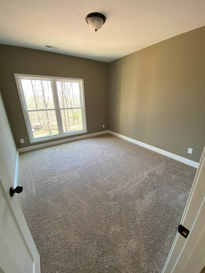 Carpeted room with white walls, large window overlooking trees, black door knob on white door, modern light fixture, and phone on nearby surface