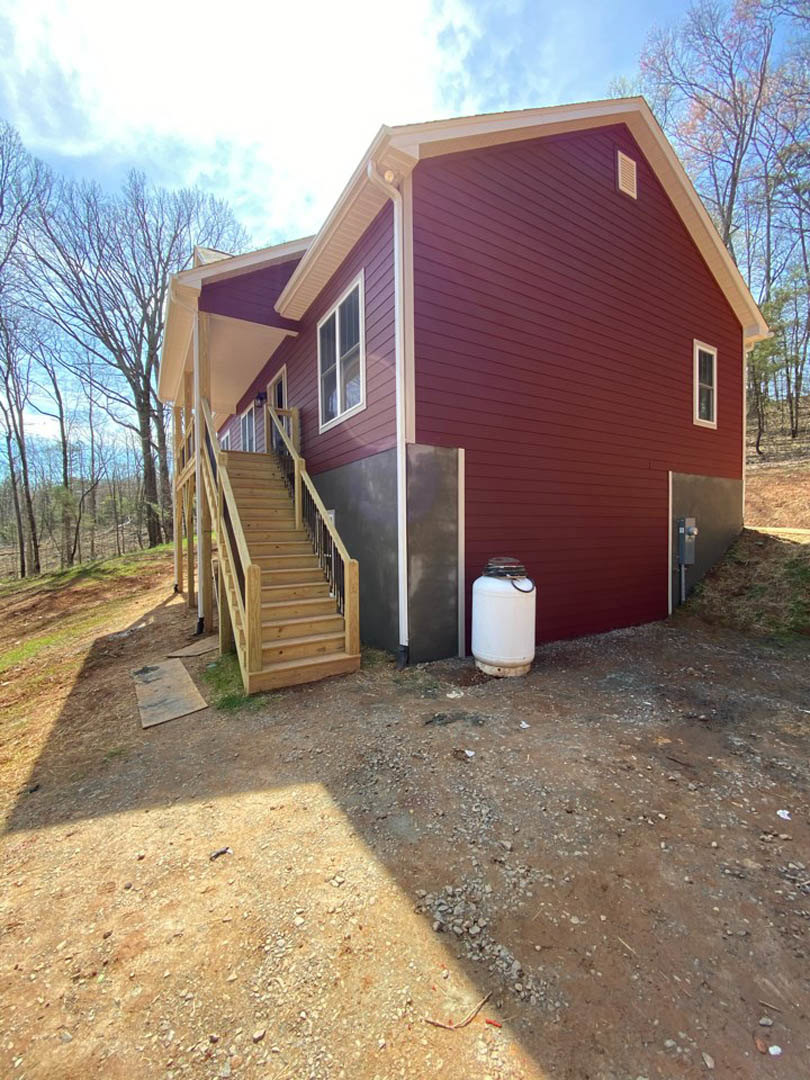 Modern home exterior with wooden staircase and metal railings, white framed window, white cylindrical canister with black ring near entry, square object on ground, surrounded by