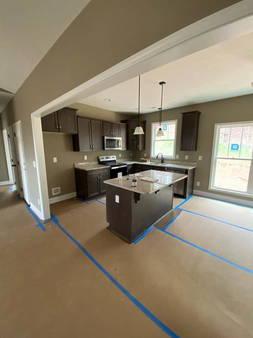 Modern kitchen with white cabinetry, stone countertop, central island holding a bottle, stainless steel microwave with glass door, recessed ceiling lights, window displaying a