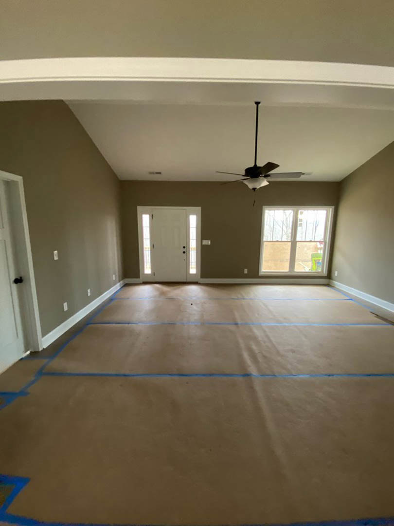 Room with blue painter’s tape outlining the ceiling and floor, white door with two glass panels, ceiling fan with light fixture, window with white trim, blue and tan carpet