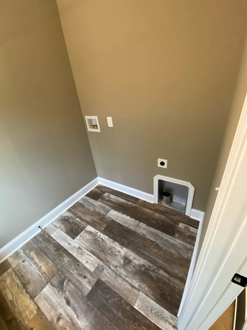 Wood floor room with a built-in dog door framed in white, small metal bin inside wall opening, white shelf mounted above, plaster walls.