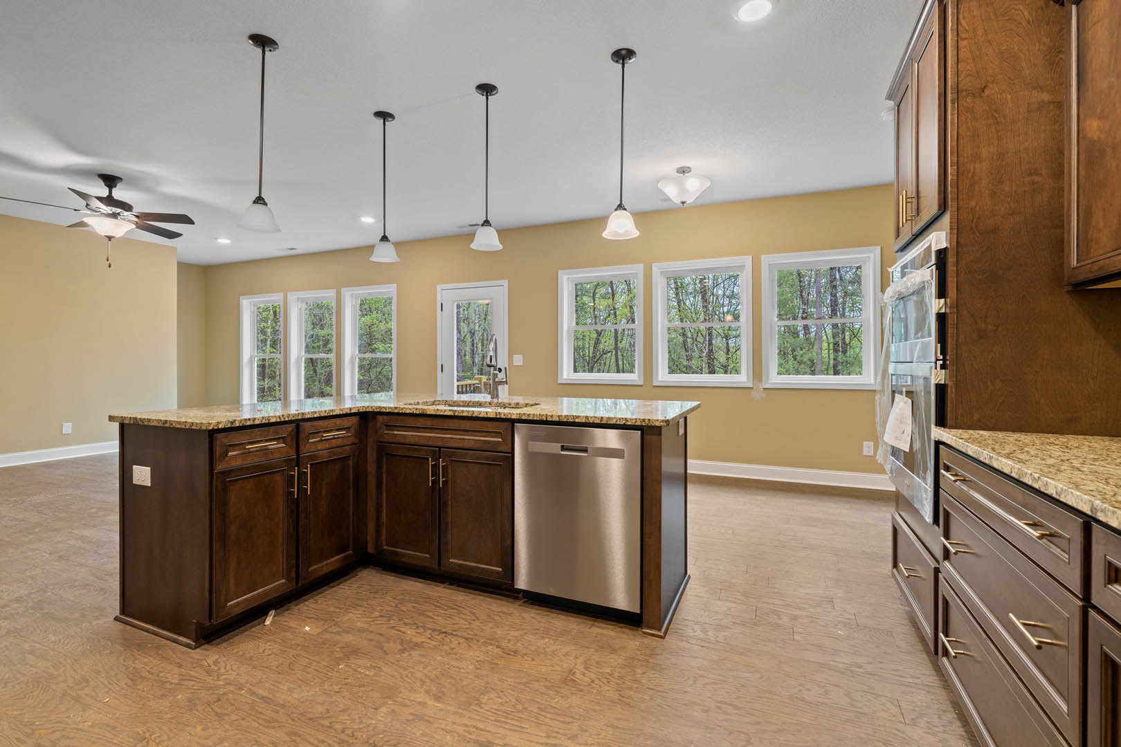 Kitchen with marble countertop, stainless steel dishwasher and stove, white cabinetry, window overlooking trees, and pole-mounted light fixture