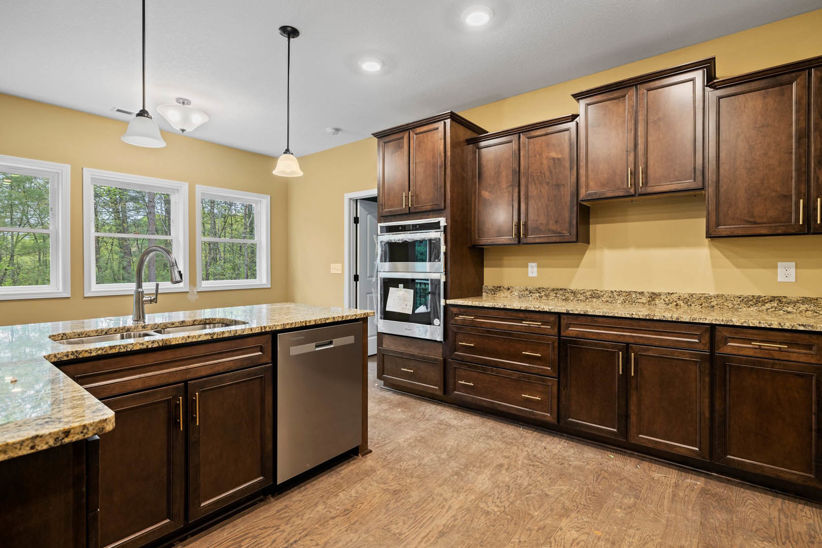 Kitchen featuring dark wood cabinetry, granite countertops, stainless steel appliances, white walls, and a window overlooking leafy trees