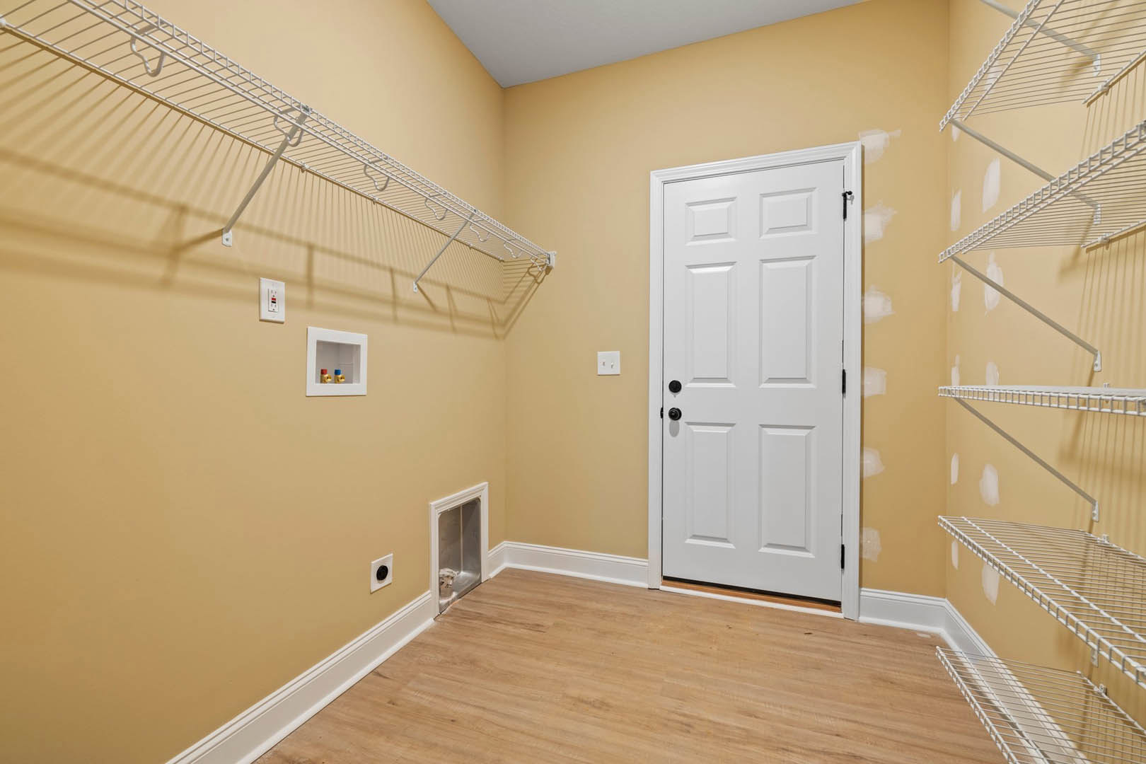 White paneled door with black hardware, wire shelving mounted on plaster wall, light wood flooring, small framed artwork and decorative objects displayed on shelves.