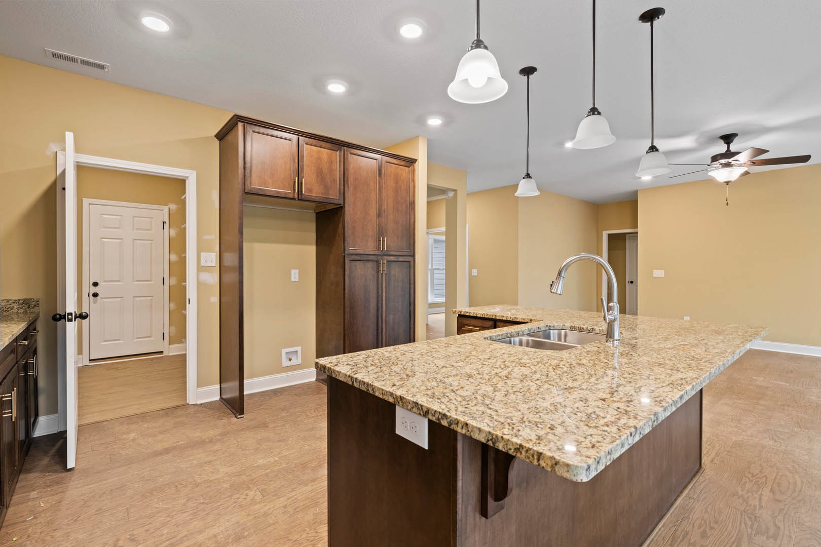 Granite kitchen island with undermount sink, wood flooring, white cabinetry, black hardware, recessed ceiling lights, and wall outlet