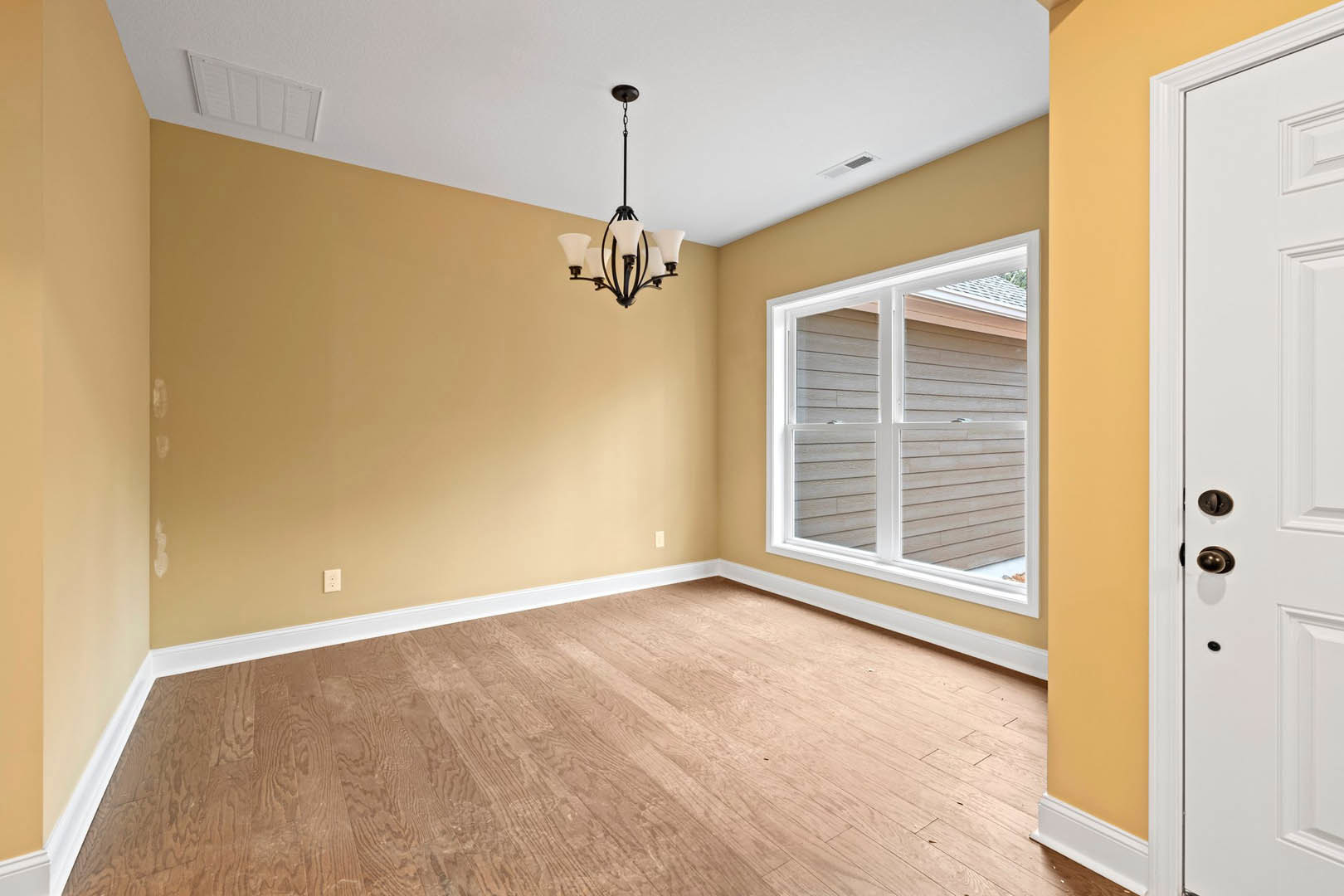 Chandelier hanging from ceiling above wooden laminate flooring, white paneled walls, white framed window, and white door with lock in custom home interior.