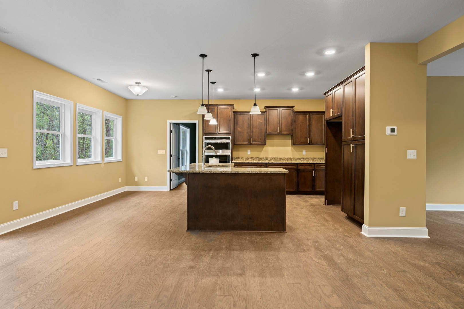 Kitchen with a central island featuring a brown base and marble countertop, hardwood flooring, white-framed windows overlooking trees, and cabinetry along the walls.