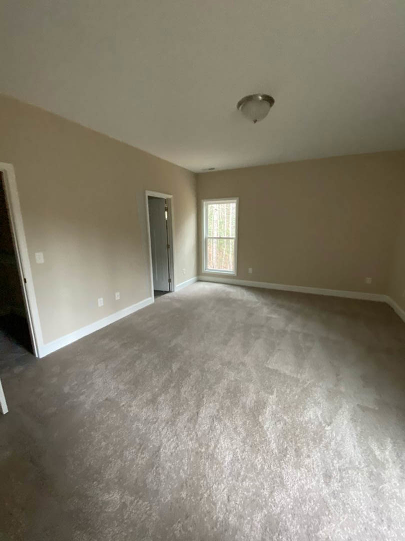 Carpeted room with white framed window, white door with silver doorknob, light fixture on smooth ceiling, neutral painted walls