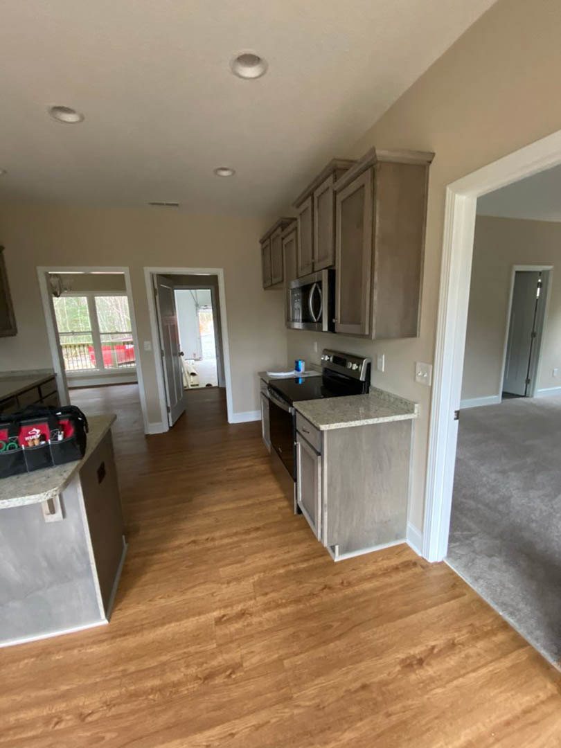 Kitchen with hardwood flooring, marble countertop on wood cabinetry, stainless steel microwave, grey painted wall, and recessed ceiling lighting.