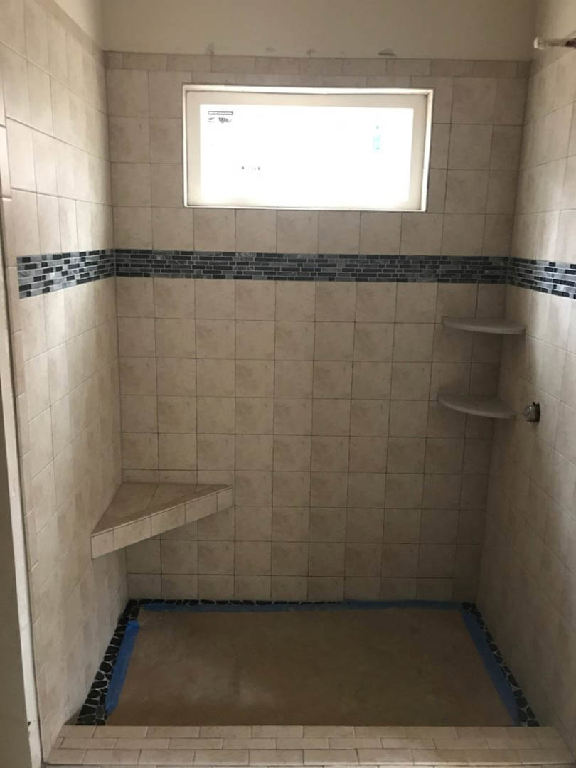 Walk-in shower with white tile walls, built-in corner shelf, and large window providing natural light