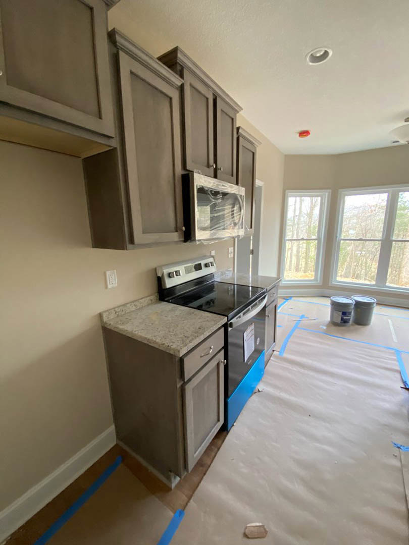Modern kitchen featuring white cabinetry, stainless steel stove and microwave, granite countertops, built-in dishwasher, large windows with tree views, and plastic containers on
